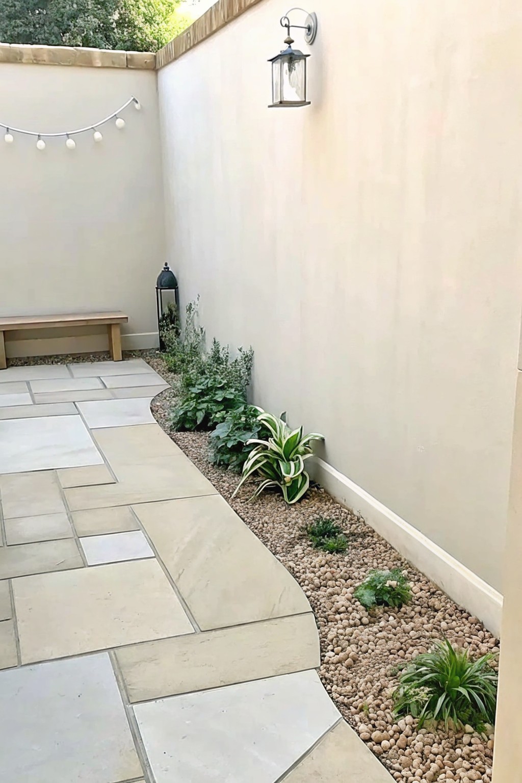 Curved stone path beside gravel garden bed with plants in beige walled courtyard.