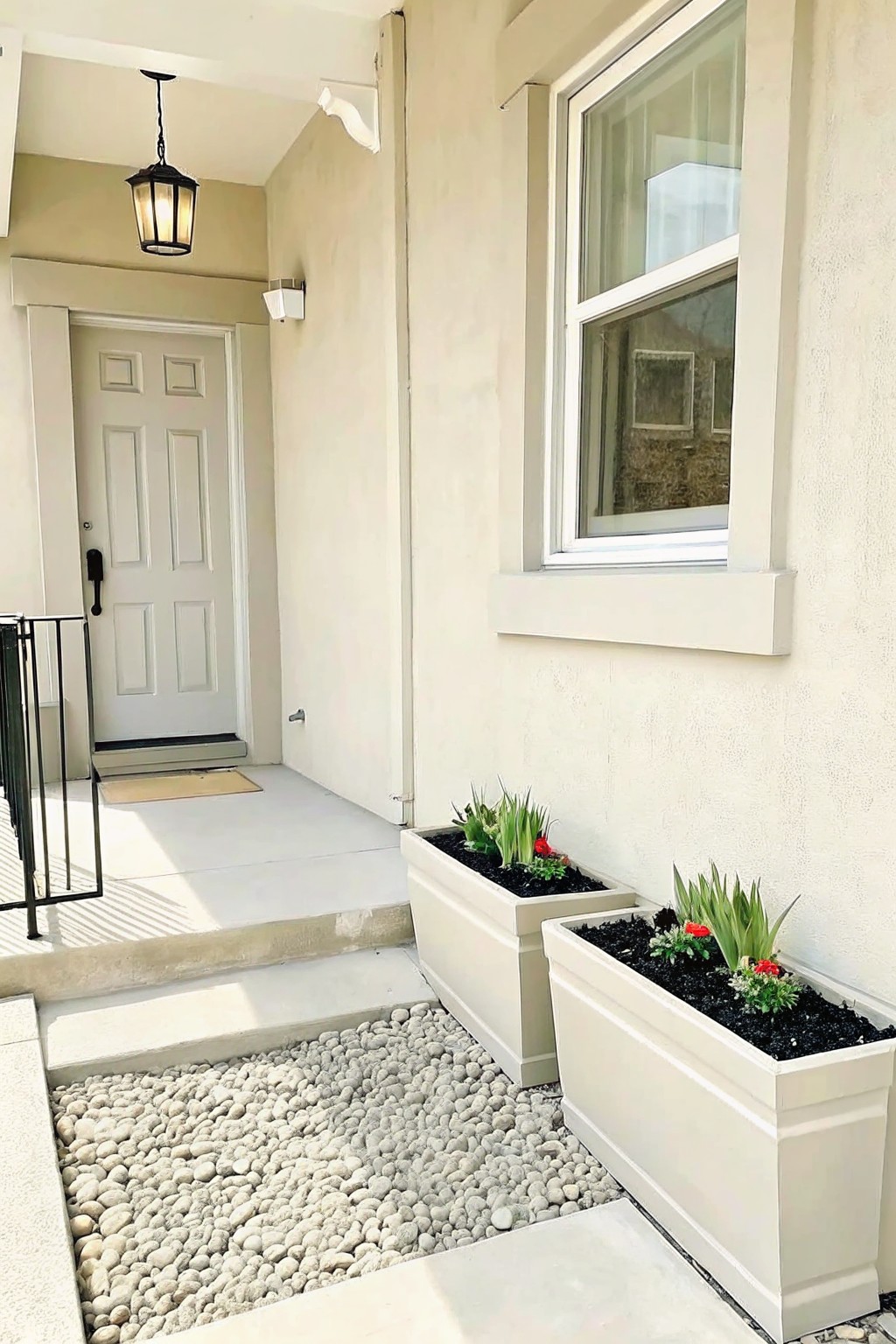 White door, steps, hanging lantern, window, and two white planters with plants