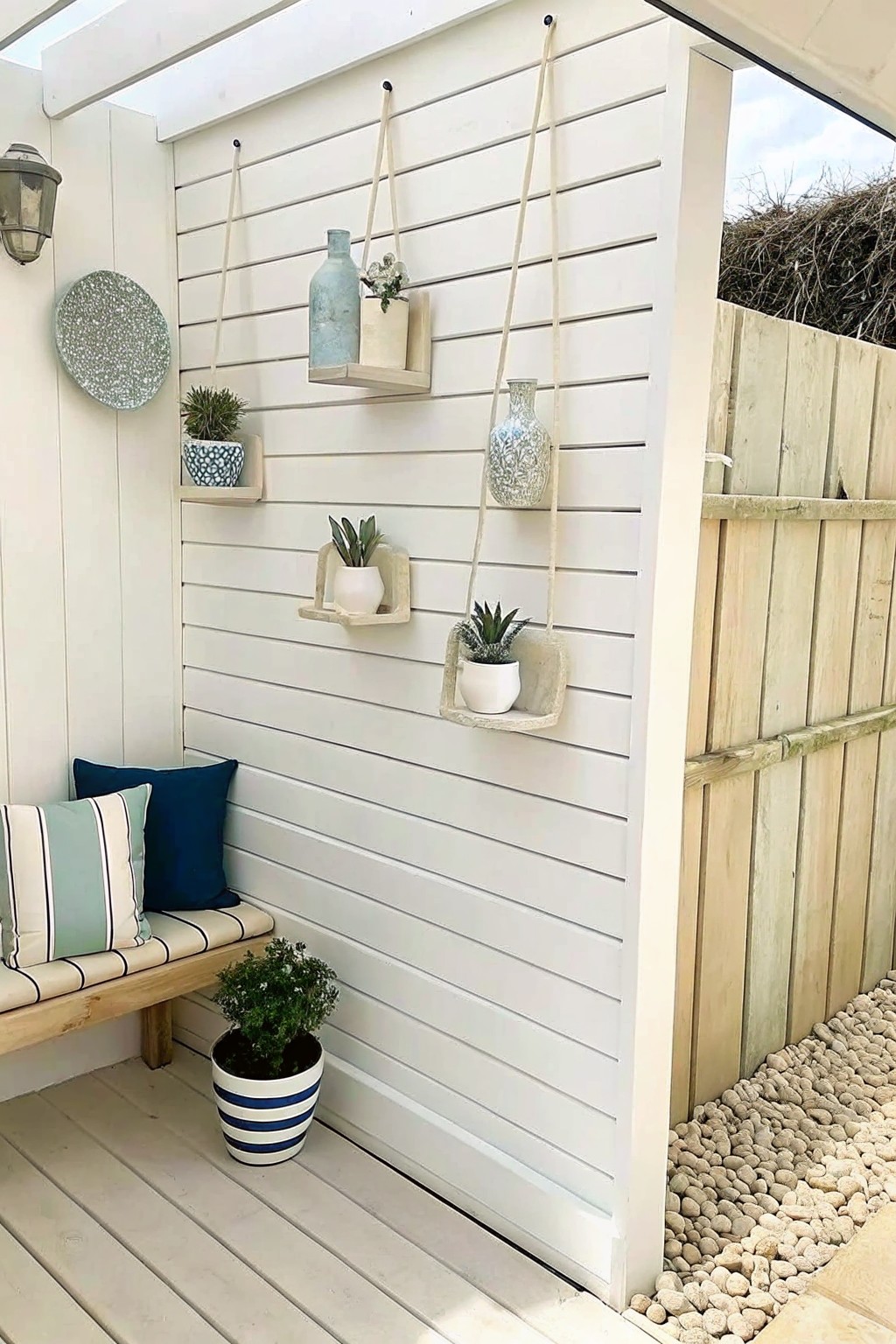 White slatted wall with hanging plant holders above wooden bench with pillows