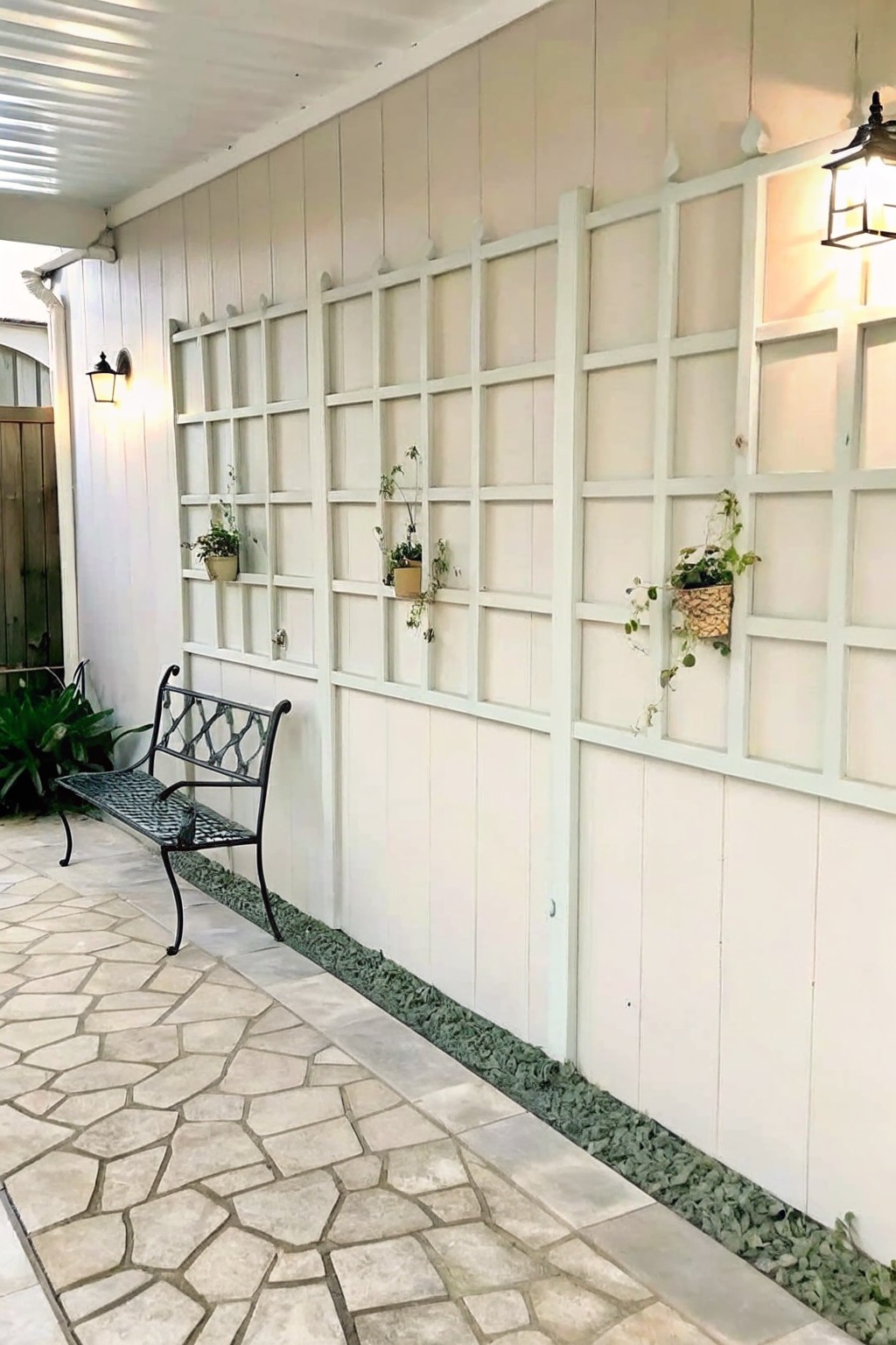 Black bench on stone patio by white lattice wall with hanging plants and lights