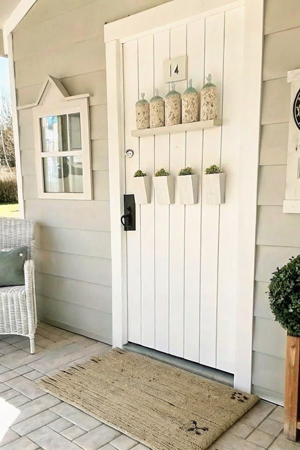 A white paneled door with four small white planters mounted in a row below a narrow shelf holding five glass jars.