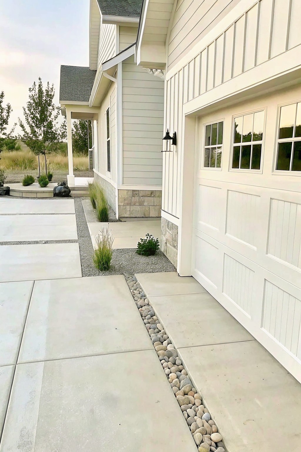 Modern white house with garage, stone accents, pebble-lined concrete driveway and landscaping