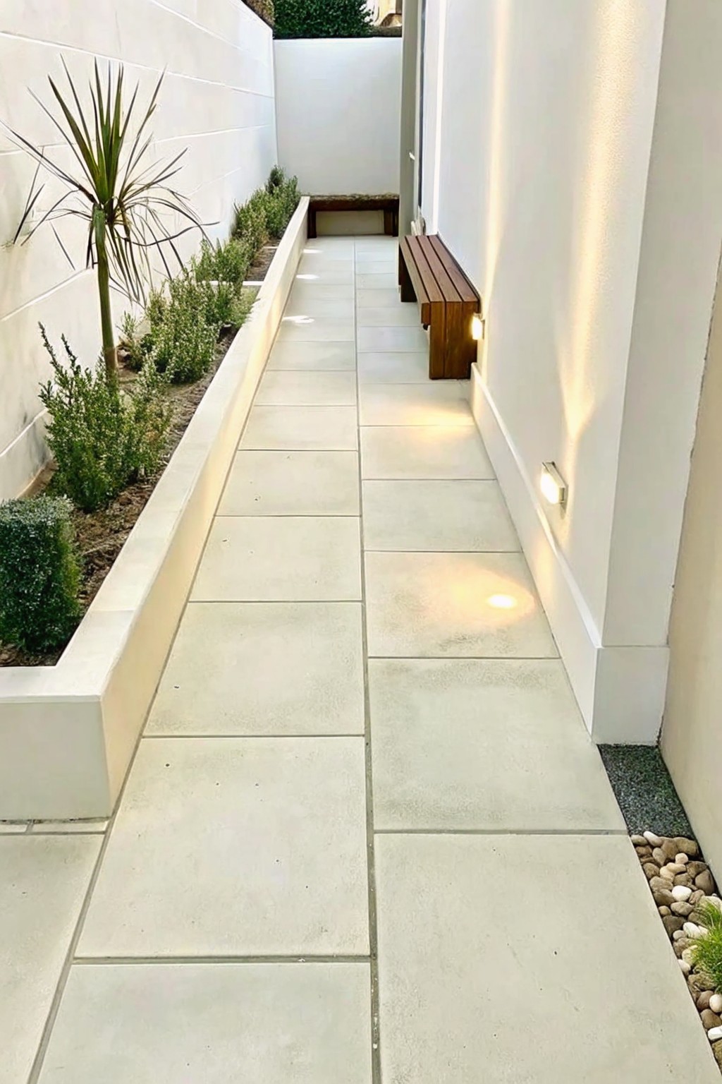 Narrow tiled walkway between white walls with wooden bench and plants