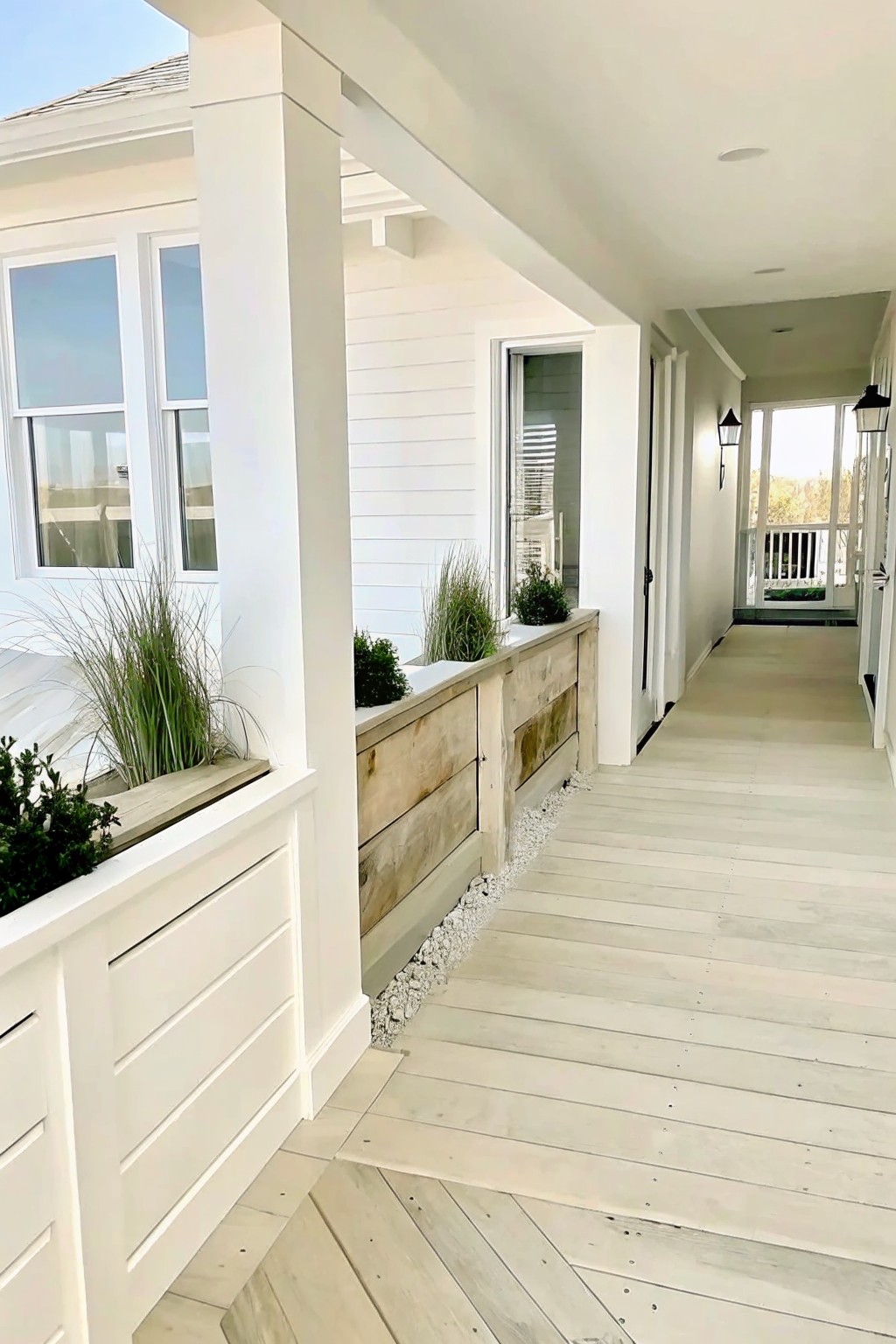 White covered porch with wooden planters, green plants, and light wooden flooring.