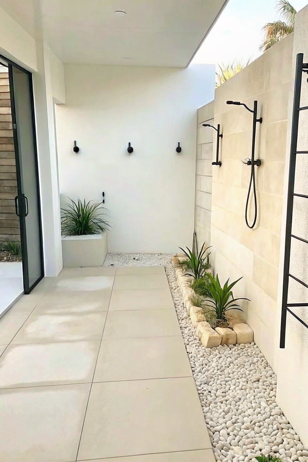 Modern outdoor shower with black fixtures on beige tiled wall beside pebble garden bed