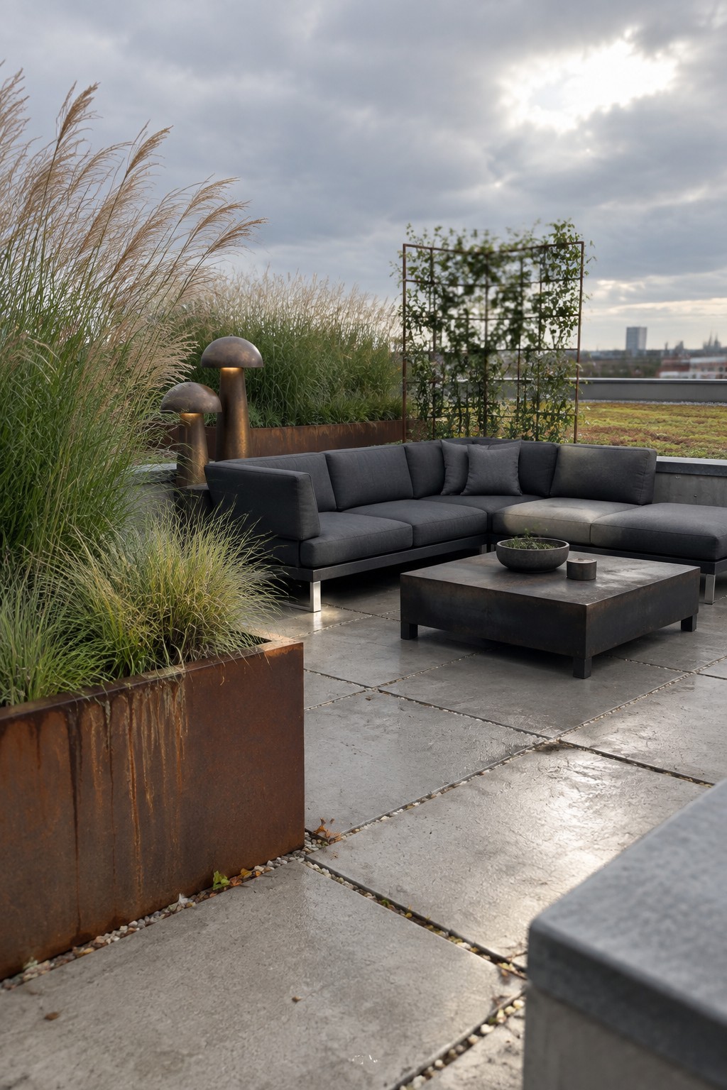 A roof terrace with a dark sectional sofa, metal coffee table, and large rectangular raised beds holding tall ornamental grasses beside the seating.