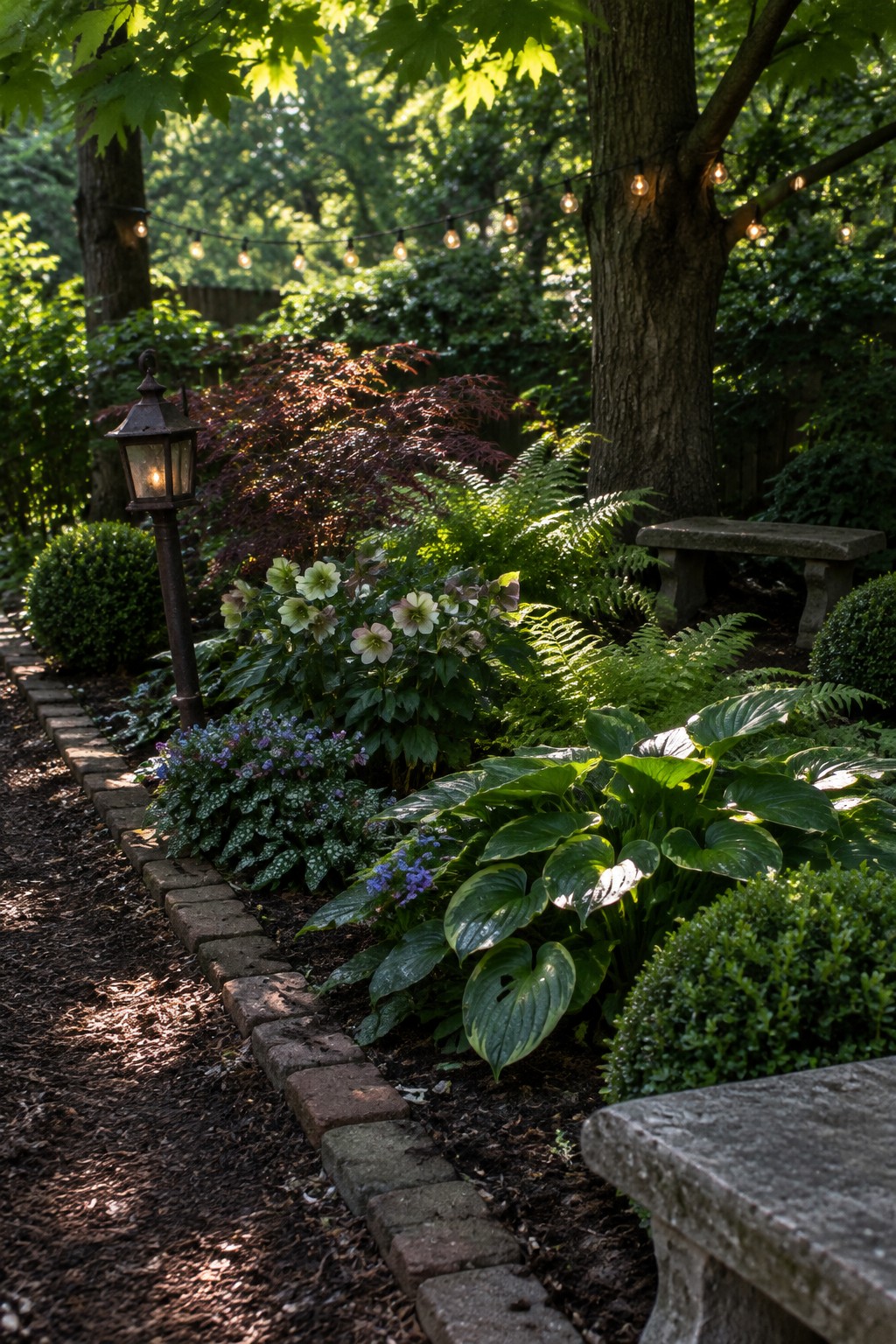 A landscaped backyard flower bed bordered by bricks, with hostas, ferns, flowering plants, and a mulched path.