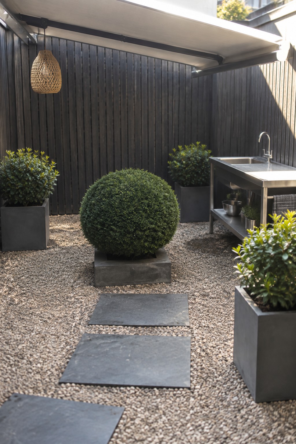 Modern gravel patio with stepping stones, potted shrubs, round bush, and stainless sink