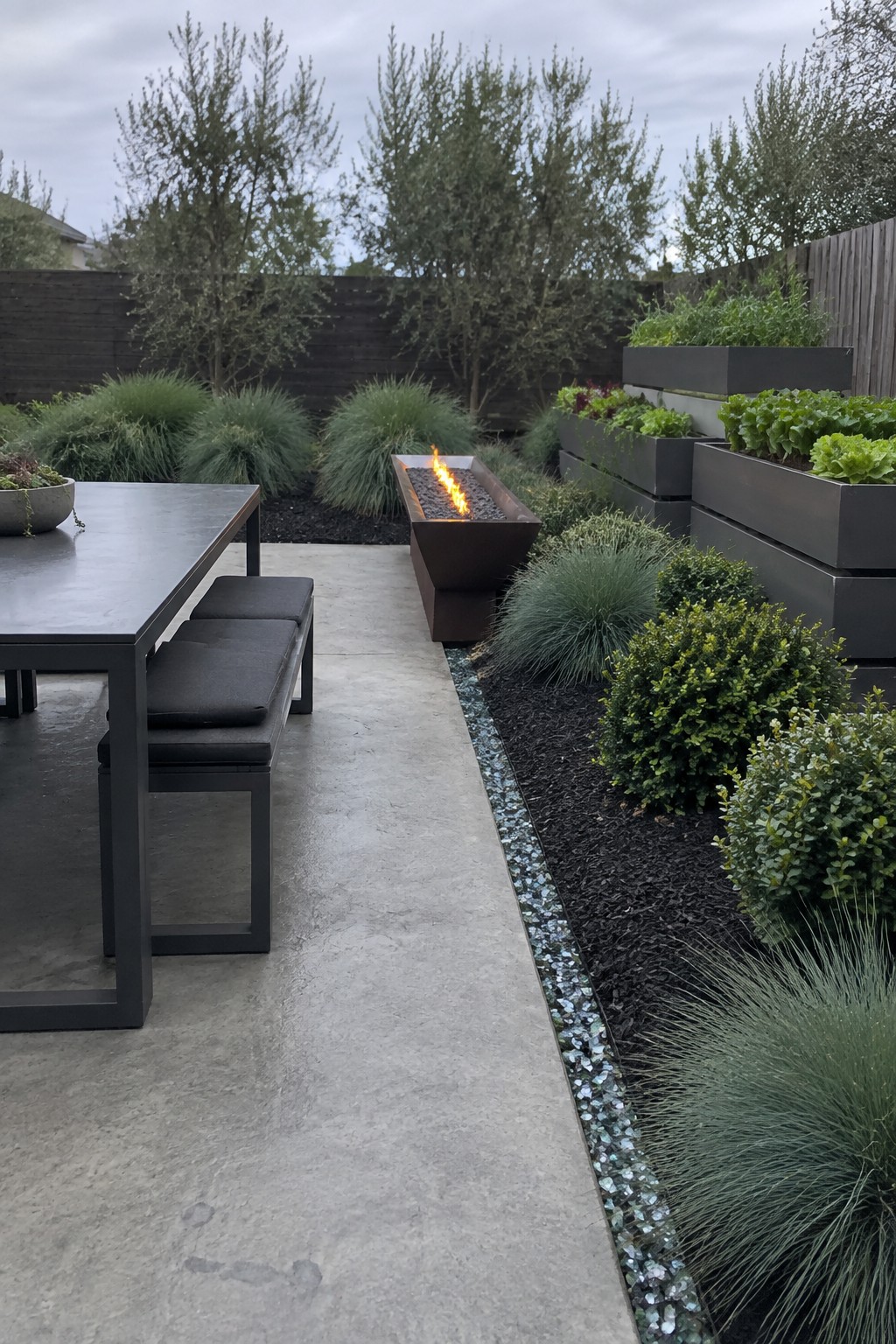 Modern patio with dining table, fire pit, raised planters, and greenery