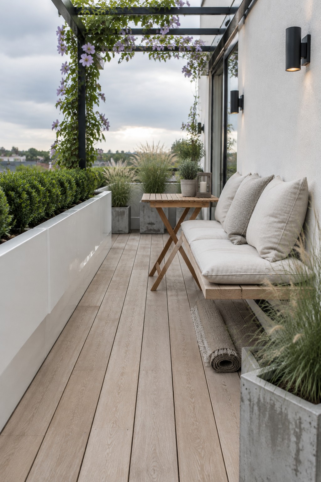 A narrow wooden balcony terrace with a built-in bench, long white planters along the left edge, a small folding table, and overhead vines with purple flowers.