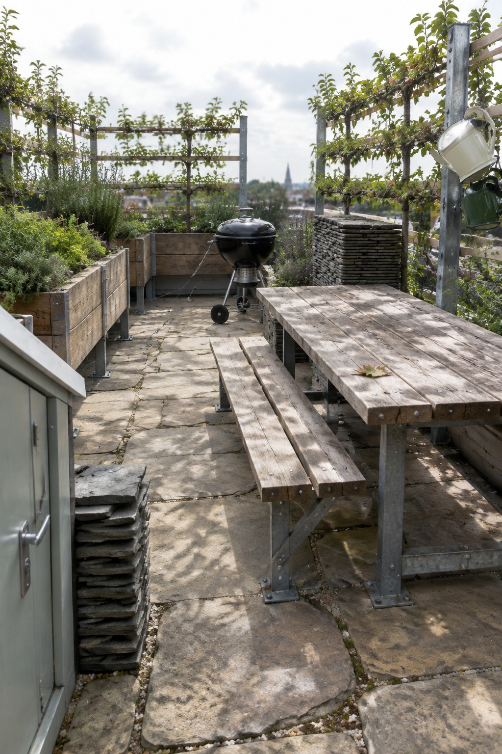 Rooftop terrace with wooden raised planters on metal supports, a picnic table, and a black grill on stone pavers.