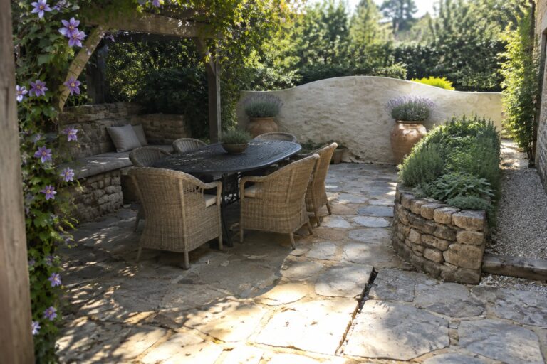 Stone patio with round table, wicker chairs, and purple flowers on pergola