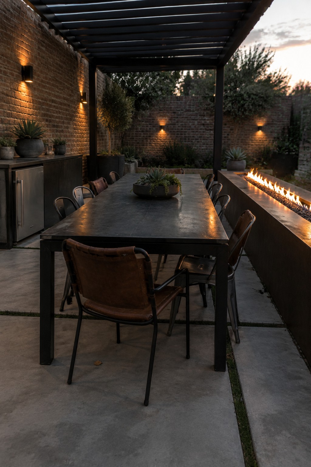Dark outdoor dining table with leather chairs beside brick wall and fire pit