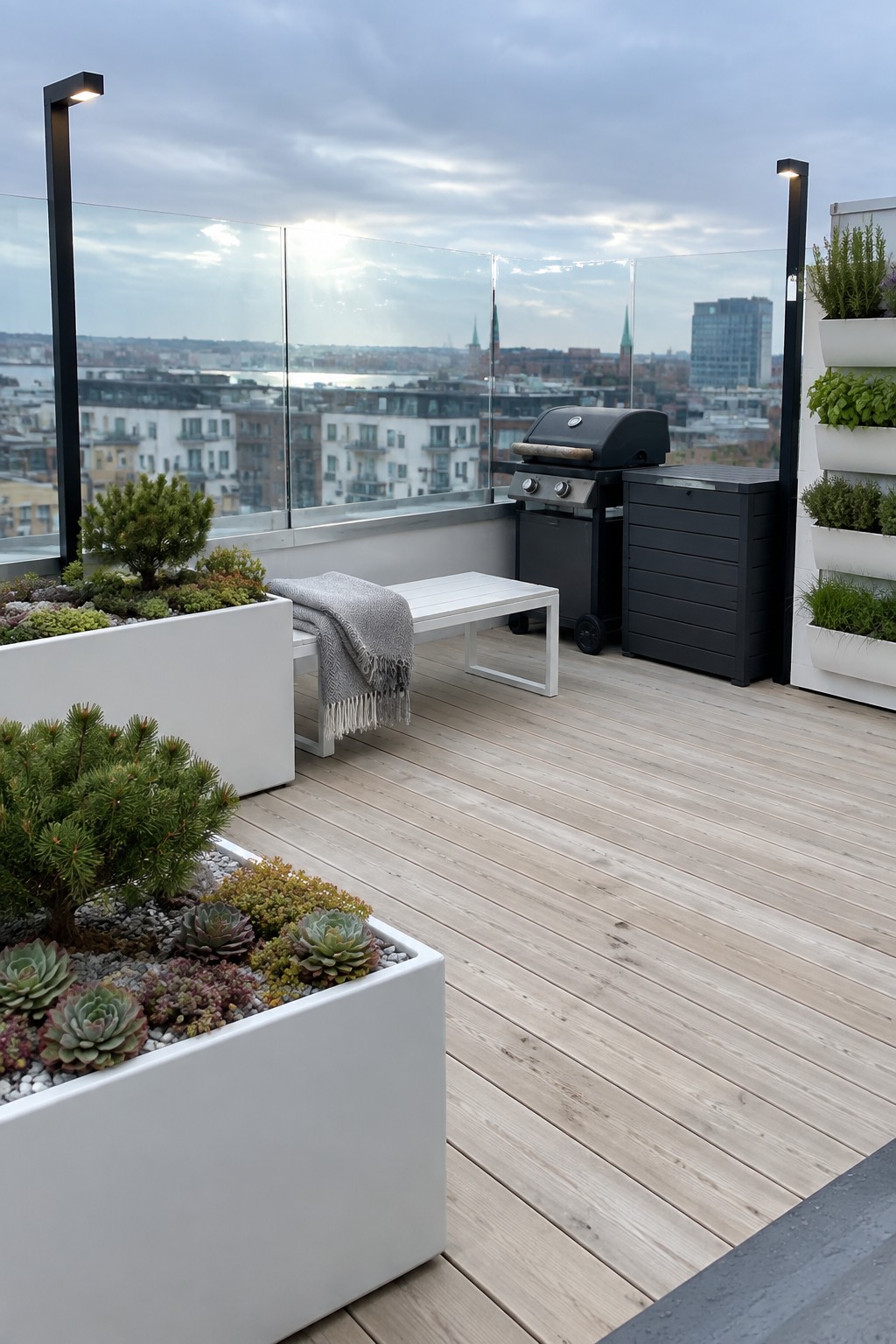 Rooftop deck with wooden flooring, white succulent planters, bench, grill, and city view.