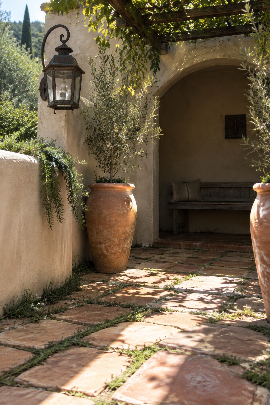 A garden path of irregular terracotta pavers with grass growing in the joints, bordered by large clay pots and leading toward a wooden bench under an arch.