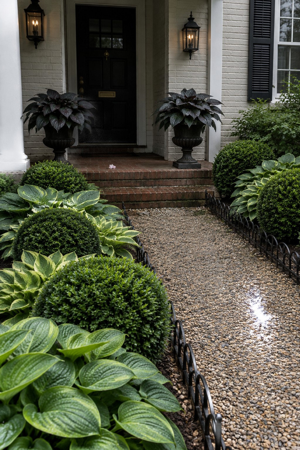 Broad-leaved hostas and rounded shrubs border a pebble path leading to brick steps and a black front door.