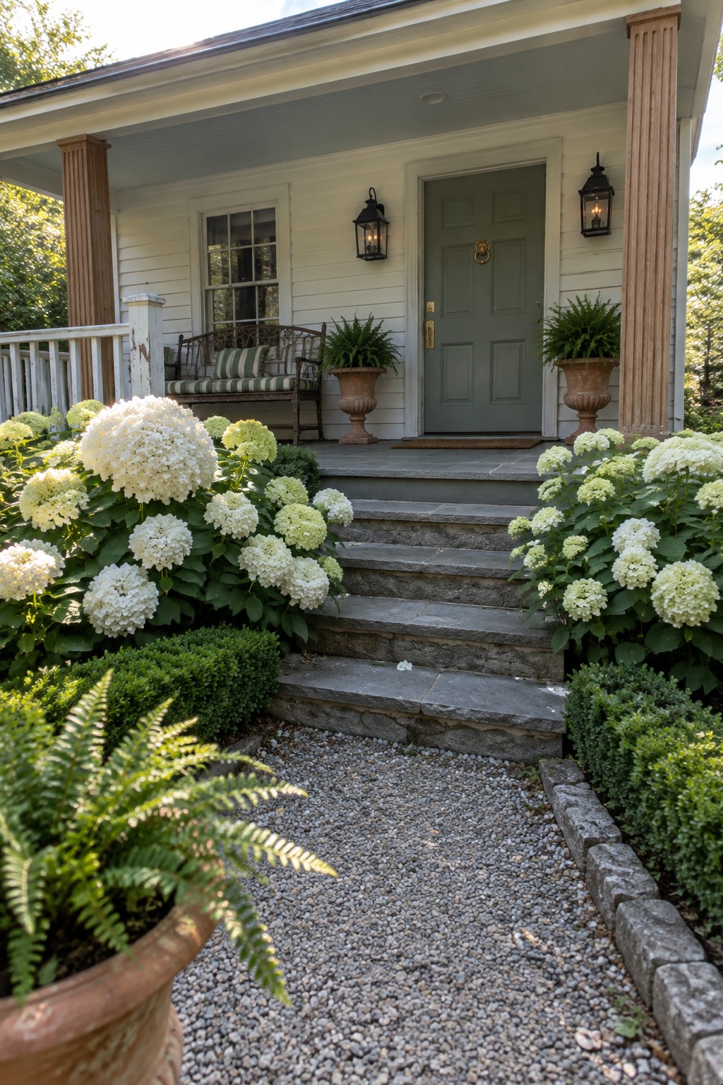 White and pale green hydrangeas line a gravel path leading to stone steps and a covered porch with a green front door.