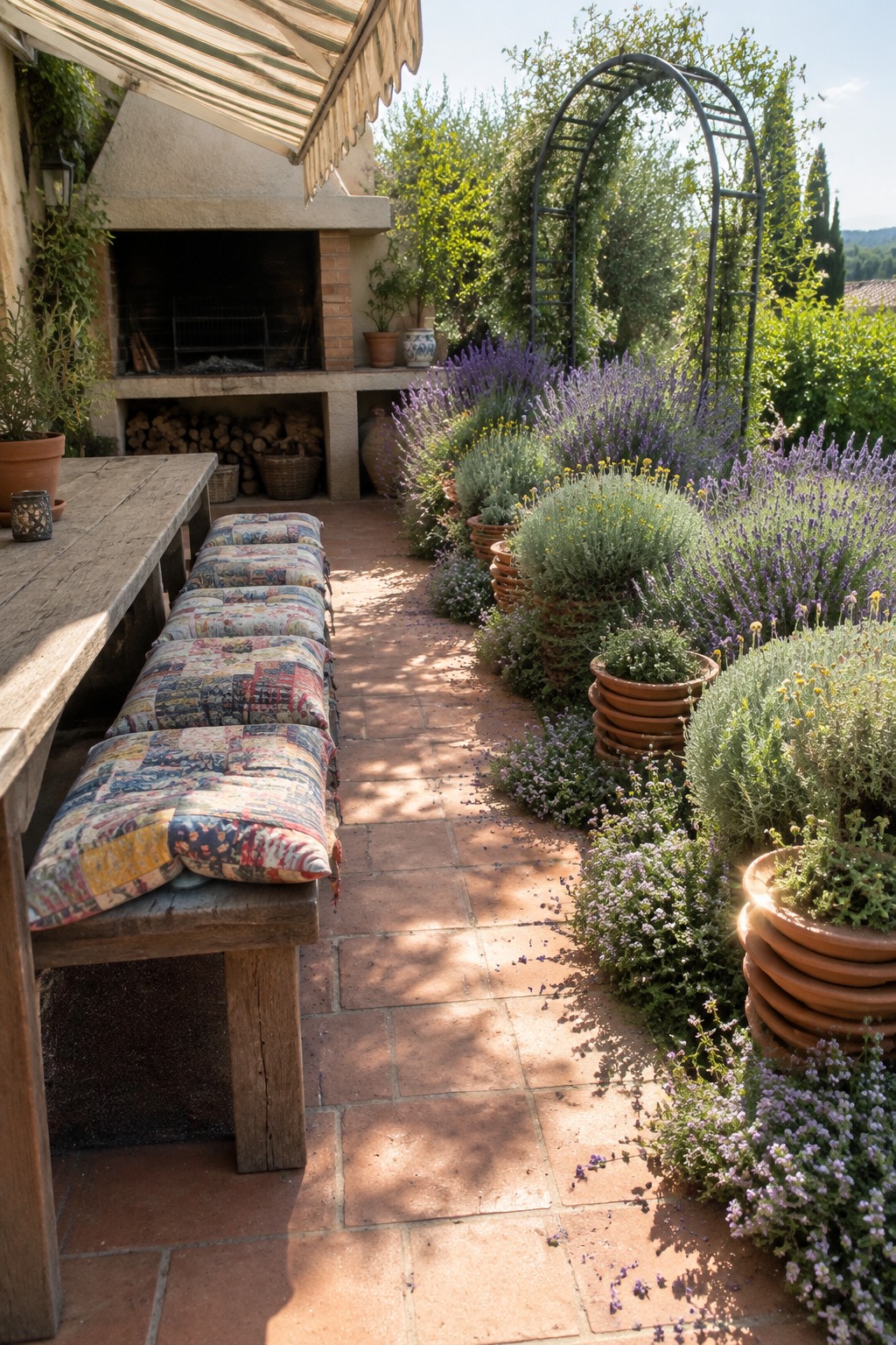 A terracotta-paved garden path runs beside dense lavender beds and a wooden bench near an outdoor fireplace.