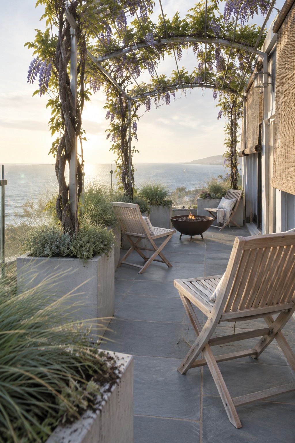 A seaside terrace with wooden chairs, planters, and a wisteria-covered pergola.