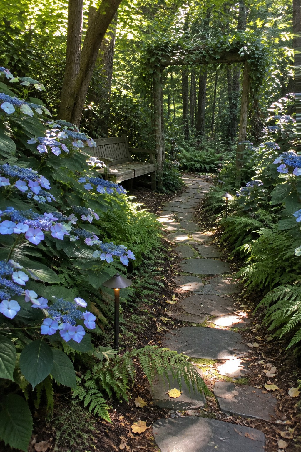 Irregular stone slabs form a path through ferns and blue hydrangeas, with a wooden bench beside it.
