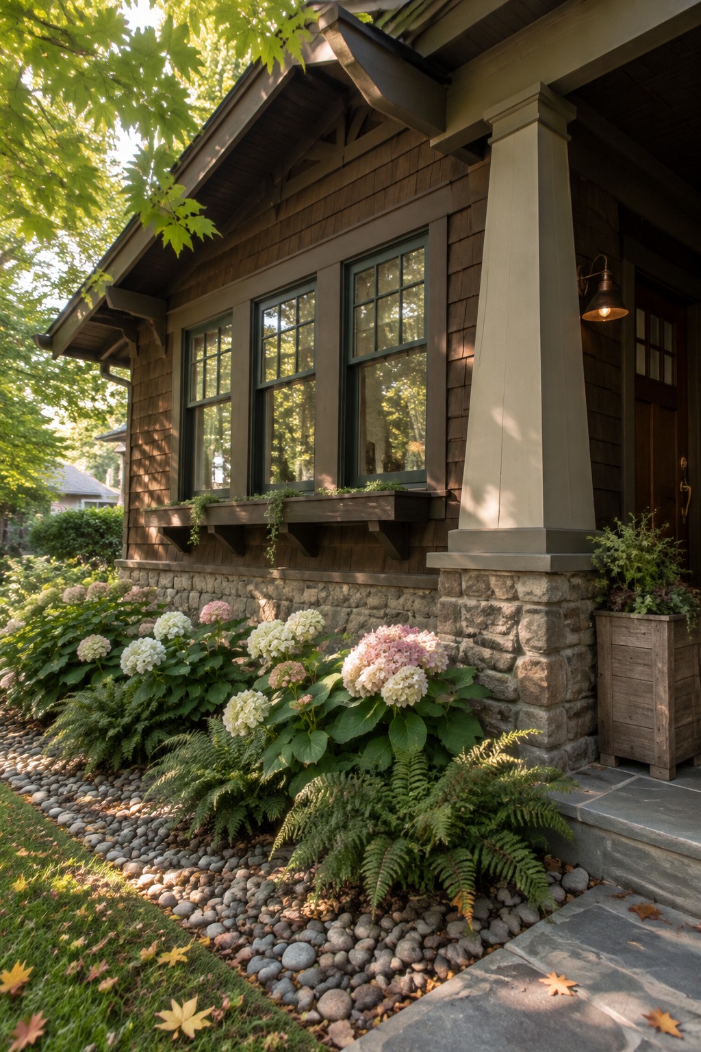 Pink and white hydrangeas and ferns grow beside a stone foundation beneath dark wood-shingled walls and windows.