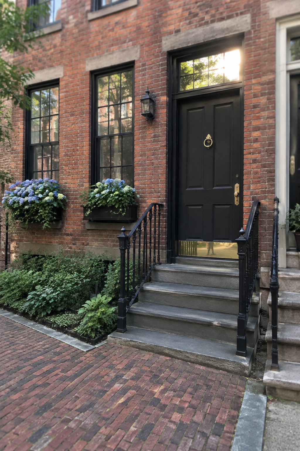 Blue and pale green hydrangeas grow in beds beside a brick walkway leading to a black front door.