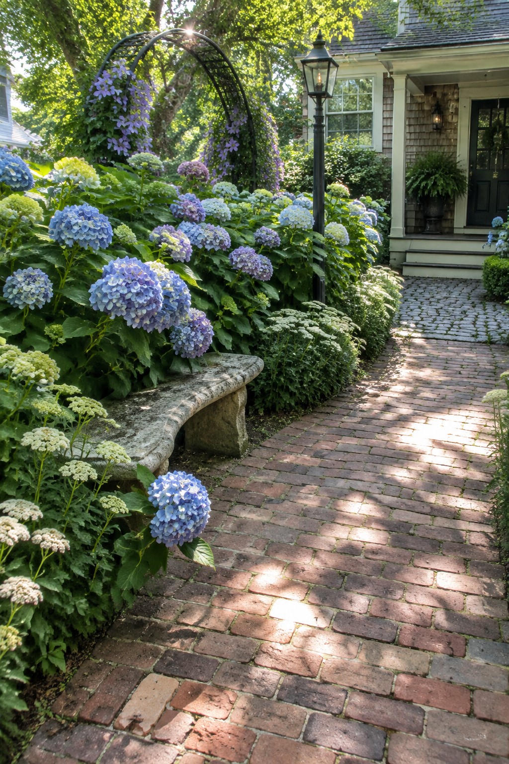A red brick walkway passes hydrangeas and other flowers beside a house.