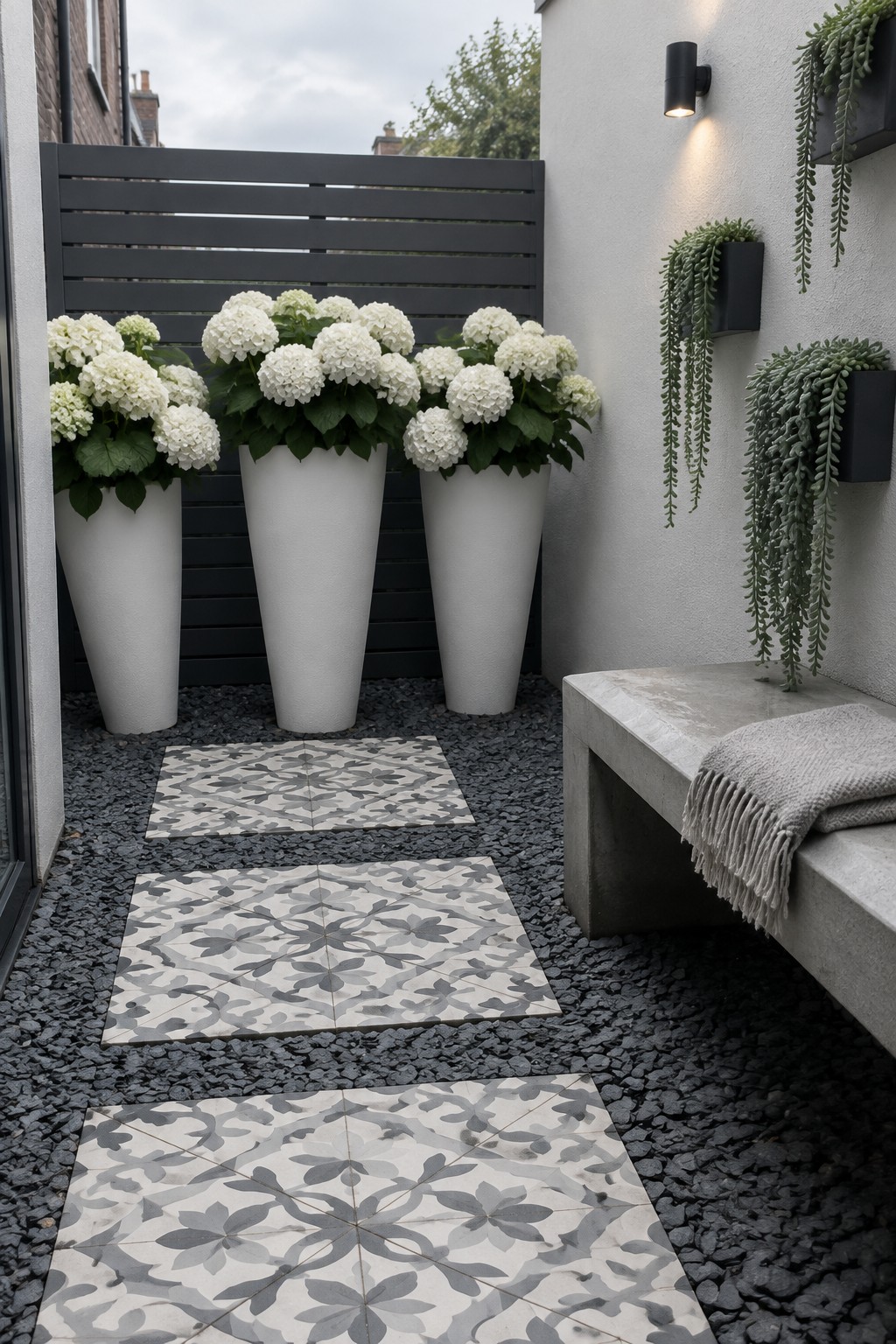 Three tall white planters filled with white hydrangeas stand beside a dark slatted fence in a gravel courtyard.