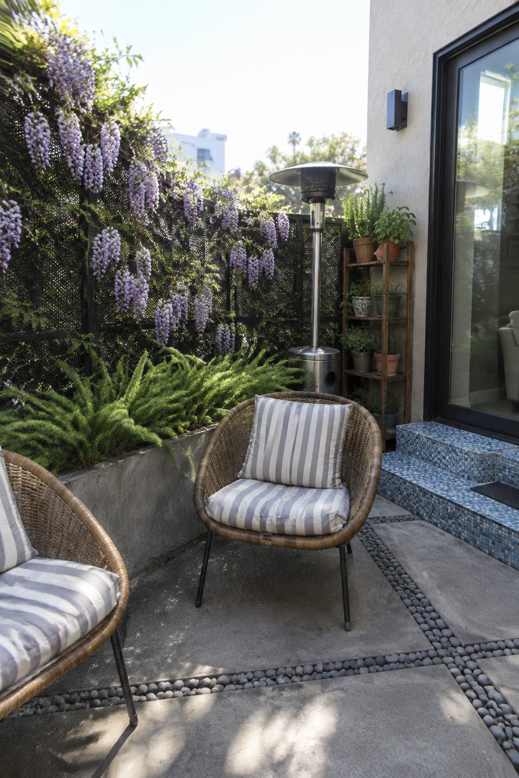 A small patio with wicker chairs beside a fence covered in purple wisteria.